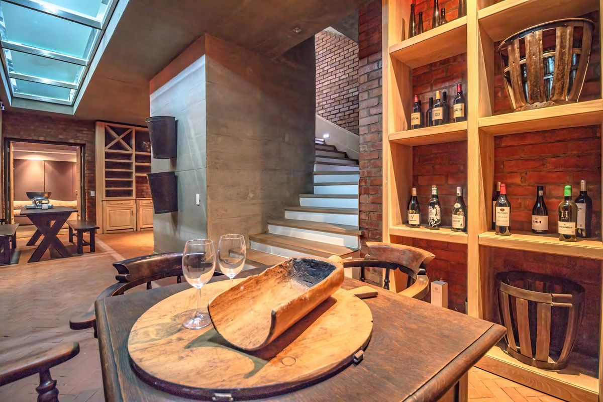 A sophisticated interior space featuring exposed brickwork, built-in timber wine shelving, a staircase, and a skylight, creating a warm and character-filled atmosphere.