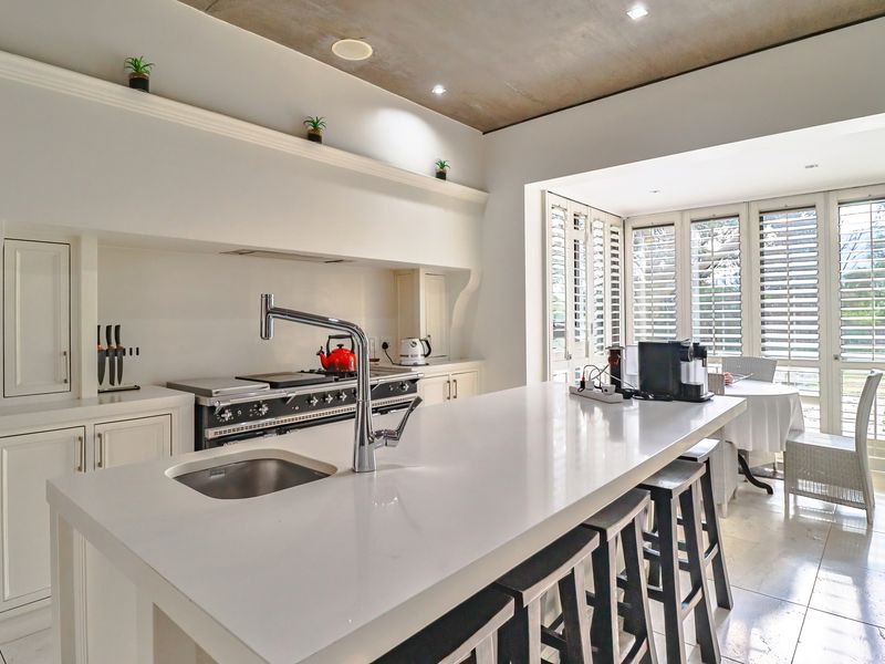 Modern open-plan kitchen featuring a large central island with stone countertop, integrated sink, and high-end range cooker, flowing into a bright dining area.