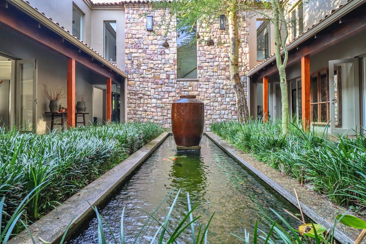 A tranquil central courtyard featuring a stone-clad feature wall, a long reflective water feature with a central urn, and covered walkways.