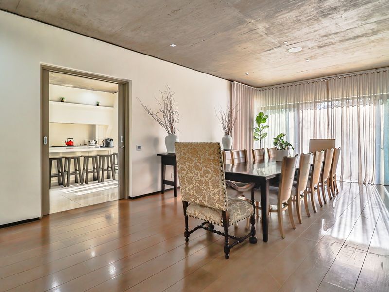 Spacious dining area featuring polished timber flooring and a striking exposed concrete ceiling, with seamless access to the adjacent kitchen.