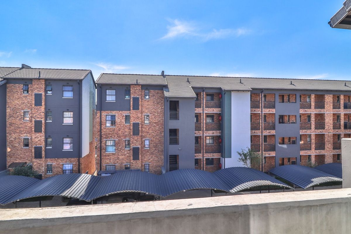 Exterior view of a modern apartment complex featuring brick and rendered facades with covered parking bays.