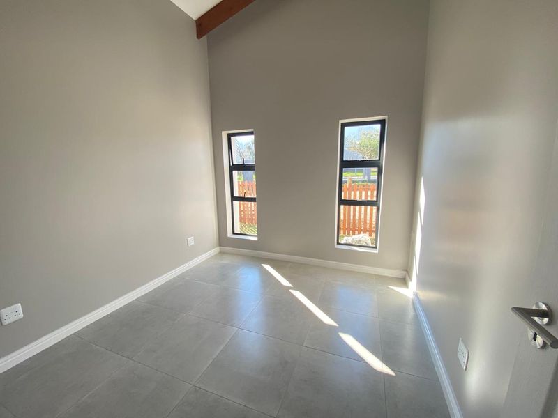 A bright, empty bedroom featuring modern grey floor tiles, neutral walls, and an exposed timber beam, offering a clean canvas for personalization.