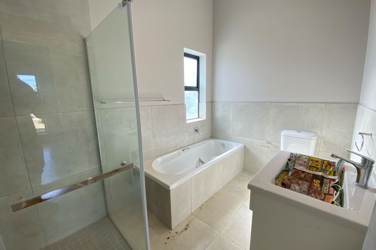 A modern bathroom featuring a glass-enclosed shower, a built-in bathtub, and a vanity basin with neutral ceramic tiling throughout.