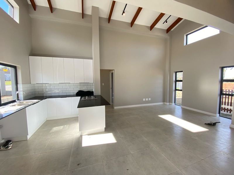 Spacious open-plan living area featuring a modern kitchen with white cabinetry, stone countertops, gas hob, and high vaulted ceilings with exposed timber beams.