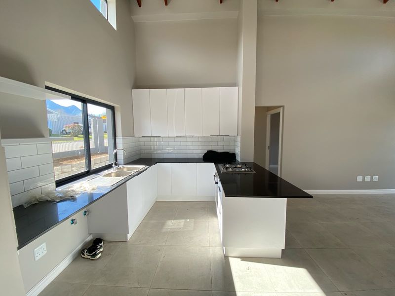 Modern kitchen featuring white cabinetry, black stone countertops, subway tile backsplash, and a built-in gas hob, set within an open-plan space with vaulted ceilings.