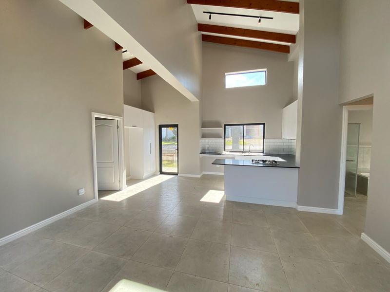 Spacious open-plan living and kitchen area featuring high vaulted ceilings with exposed timber beams, modern cabinetry, and a gas hob.
