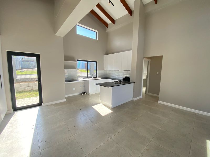 Modern, open-plan kitchen featuring high ceilings with exposed timber beams, sleek white cabinetry, stone countertops, and a gas hob, finished with neutral floor tiles.