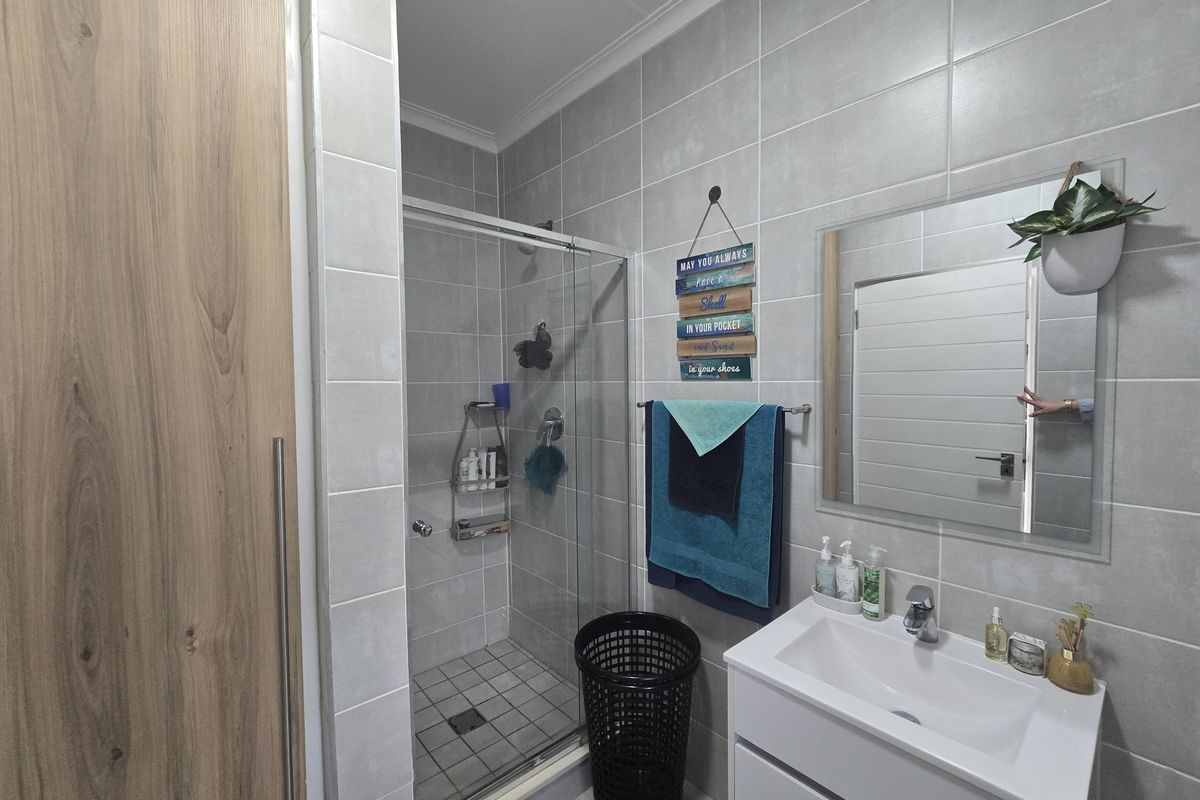 Modern bathroom featuring a glass-enclosed shower, wall-mounted vanity with basin, and neutral grey wall tiling.
