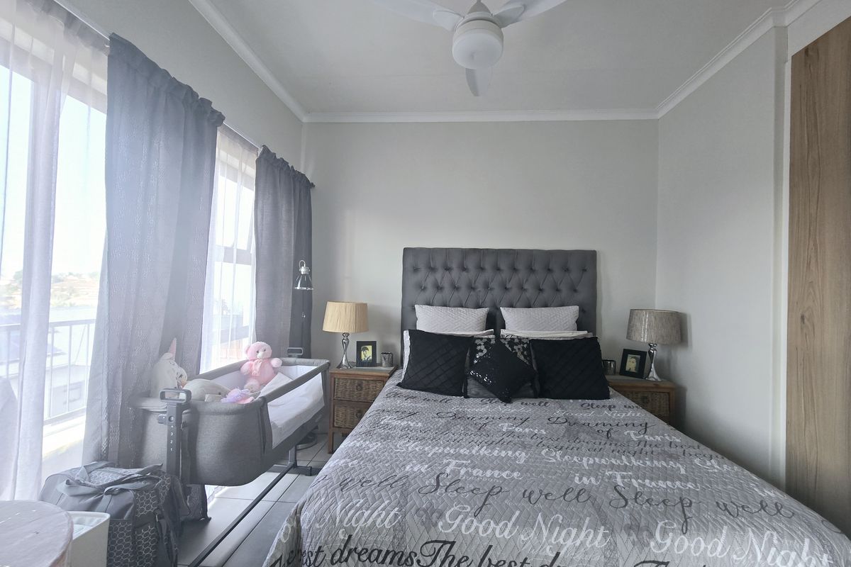 A well-maintained bedroom featuring a ceiling fan, tiled flooring, and large windows providing natural light and access to a balcony.