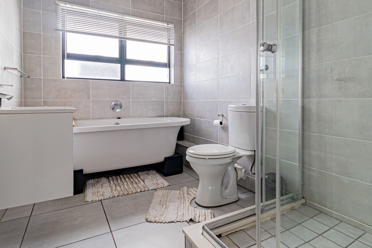 A functional bathroom featuring a freestanding bathtub, a separate glass-enclosed shower, a toilet, and a vanity, finished with neutral wall and floor tiling.