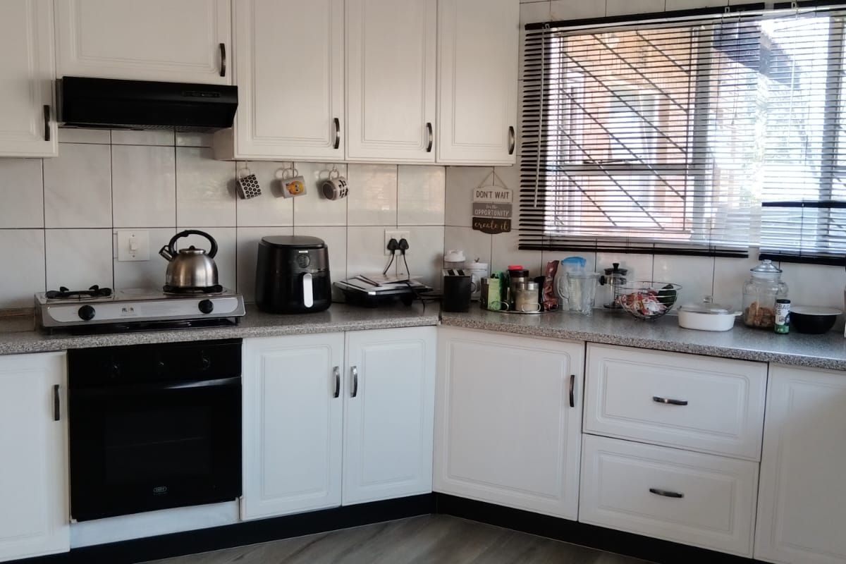 A functional kitchen featuring white cabinetry, a built-in oven, gas hob, extractor fan, and tiled splashbacks with modern wood-look flooring.