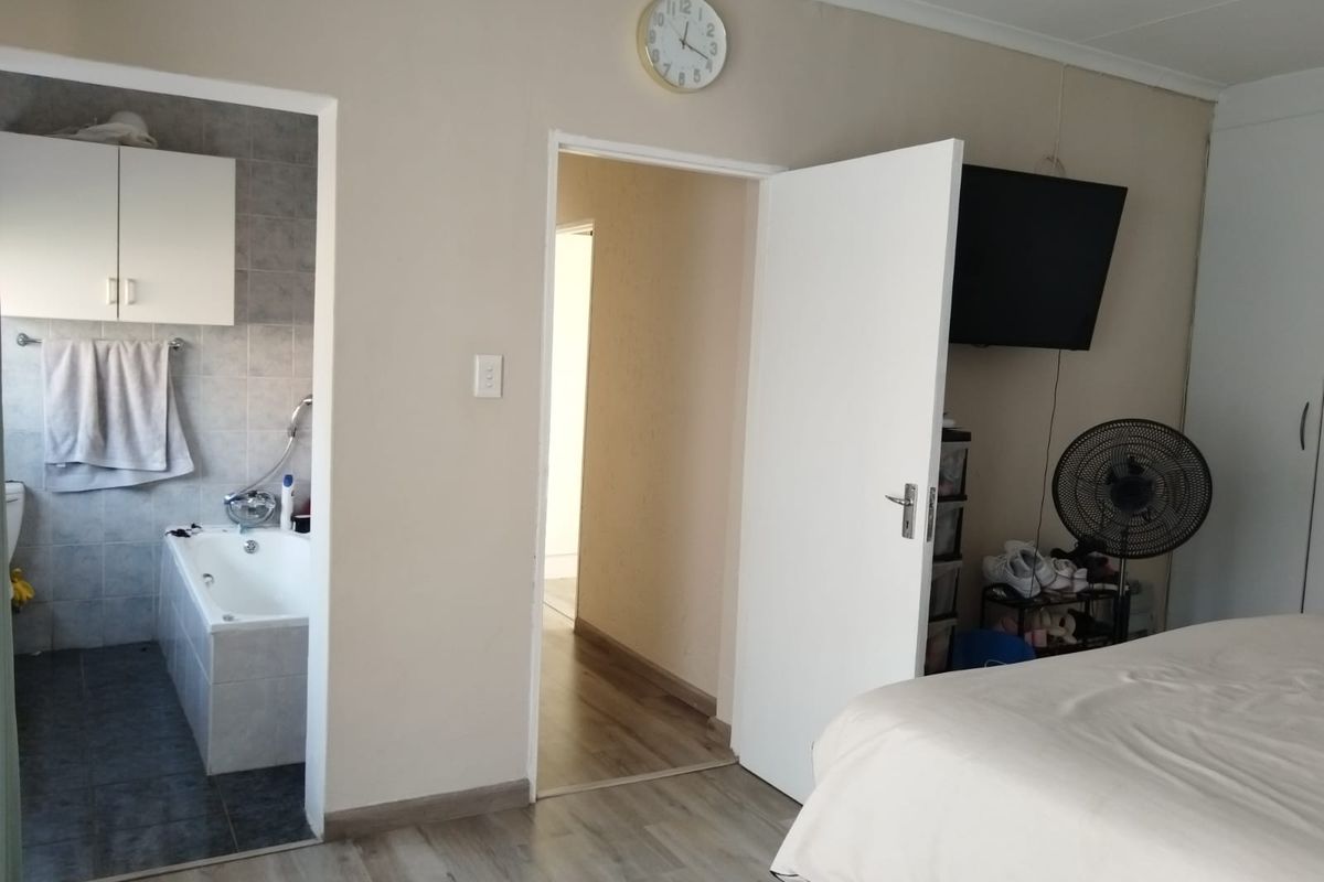 A bedroom featuring laminate flooring and an en-suite bathroom with a built-in bathtub and tiled finishes.
