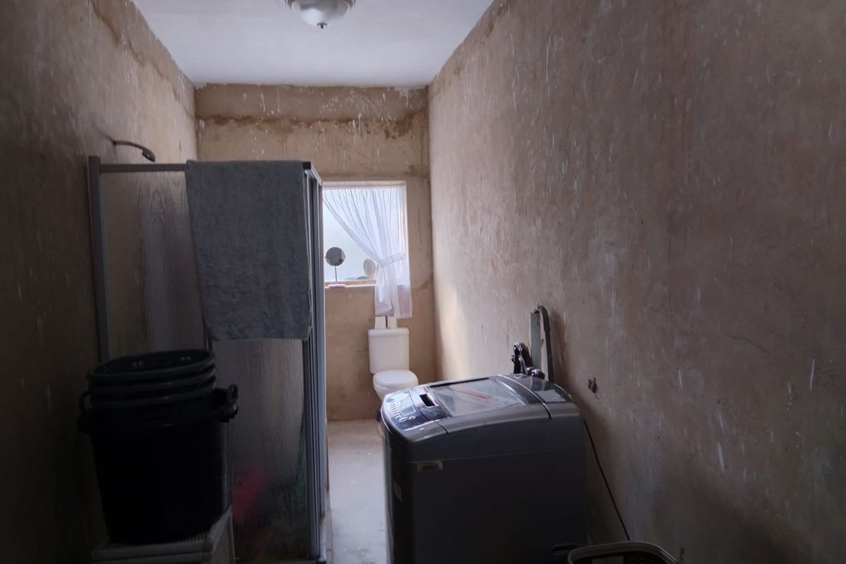 A functional bathroom and laundry area featuring a shower enclosure, toilet, and laundry plumbing connections, currently requiring significant wall finishing and cosmetic renovation.