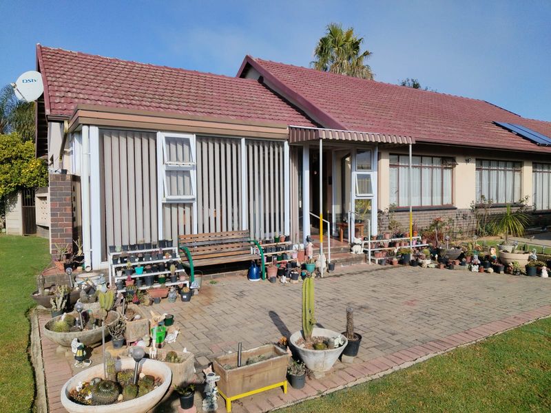 Front elevation of a single-story house featuring a tiled roof, paved patio area, and established garden entrance.