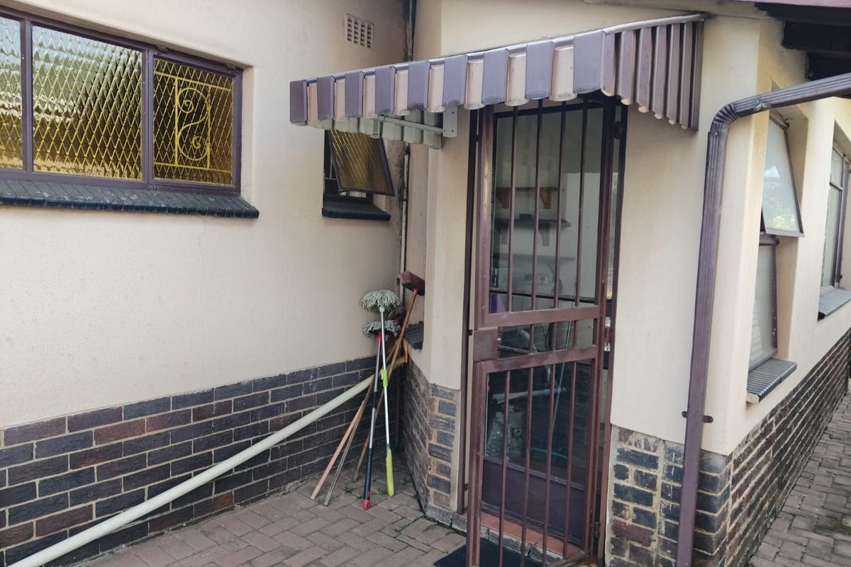 Rear exterior view showing a paved area, security gate, and protective awning over the entrance.