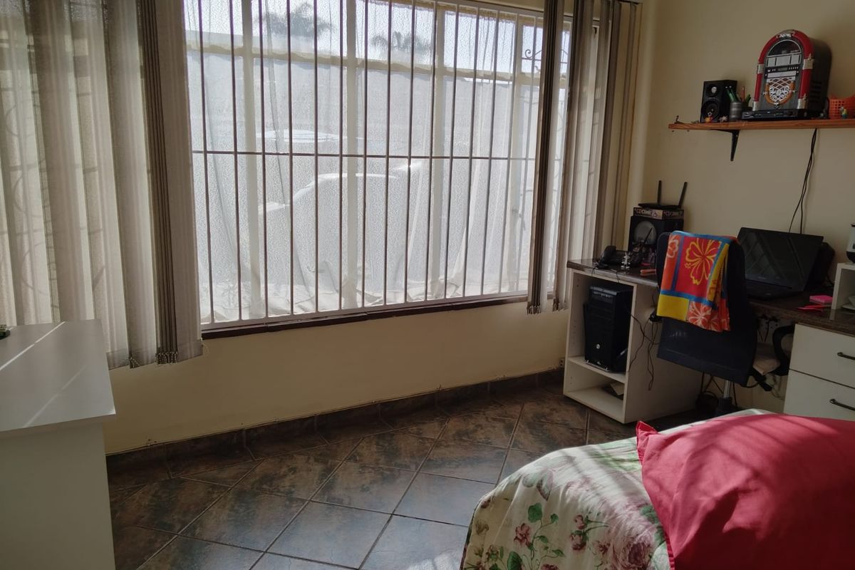 A bedroom featuring tiled flooring and a large window fitted with security bars, providing natural light.