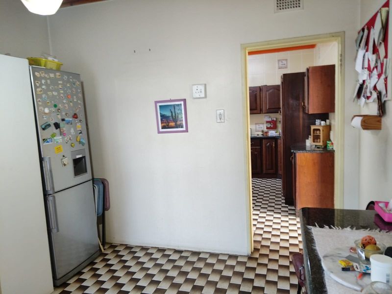 A functional kitchen area featuring checkerboard flooring and traditional wooden cabinetry, with a clear view into an adjoining scullery or secondary prep space.