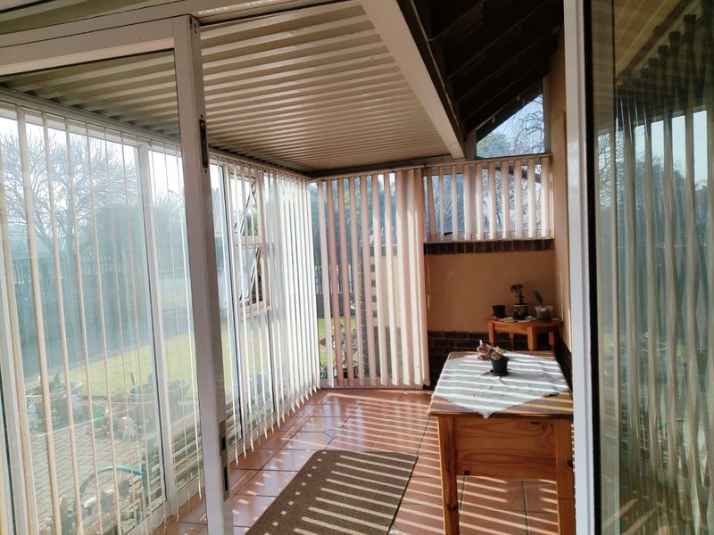 A covered patio area featuring tiled flooring, sliding glass doors, and vertical blinds, providing a functional transition space between the interior and the garden.