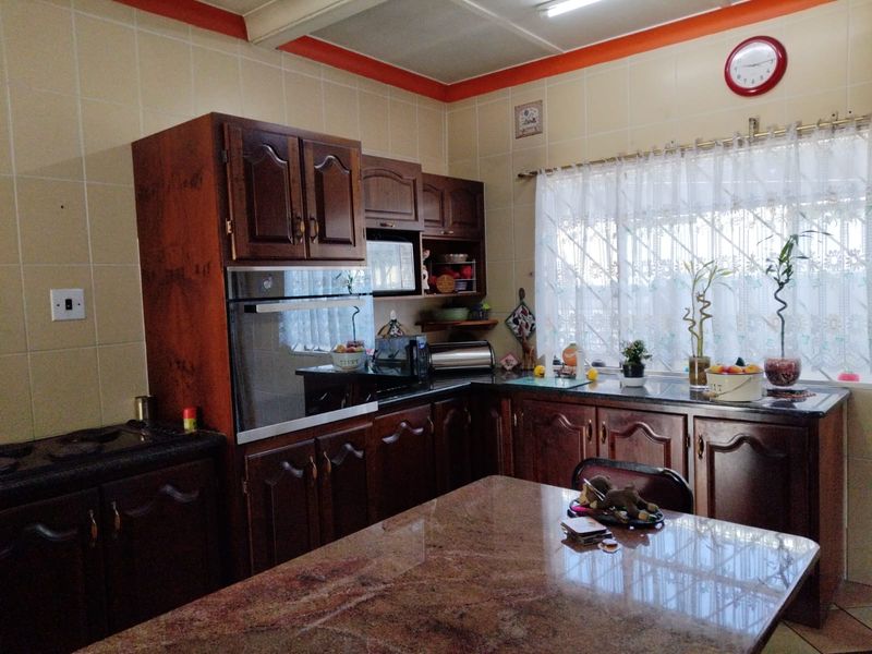 A functional kitchen featuring dark wood cabinetry, granite countertops, and tiled walls, offering a traditional layout with built-in oven and ample storage space.