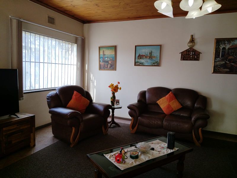 A living room featuring a timber ceiling, tiled flooring, and large windows with security bars, offering a traditional and functional living space.