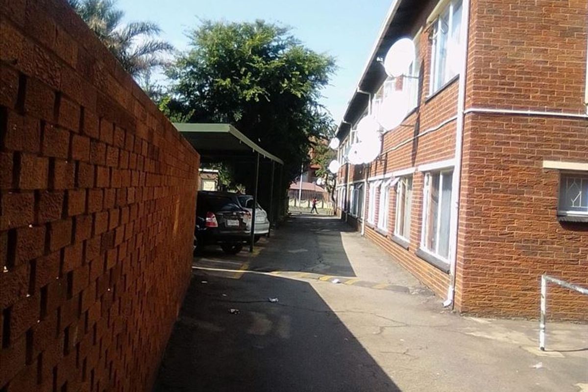 Exterior view of the apartment complex side access, featuring brick facade, paved driveway, and covered parking bays.