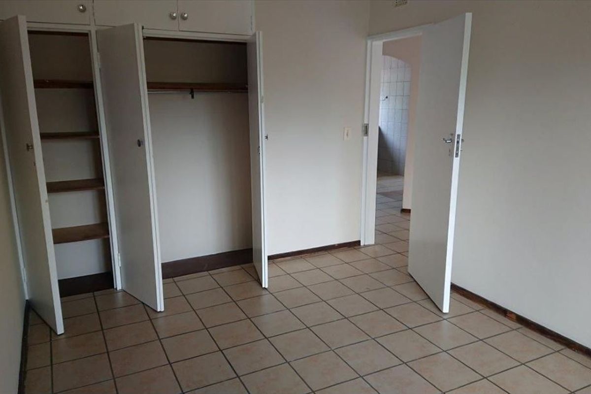 An empty bedroom featuring built-in storage cupboards, tiled flooring, and a doorway leading to an adjacent space.