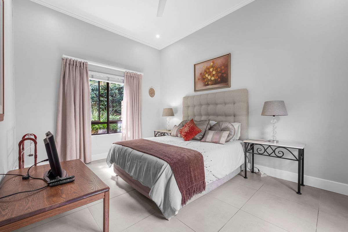 A well-maintained bedroom featuring neutral tiled flooring, high ceilings with crown molding, and a large window providing natural light.