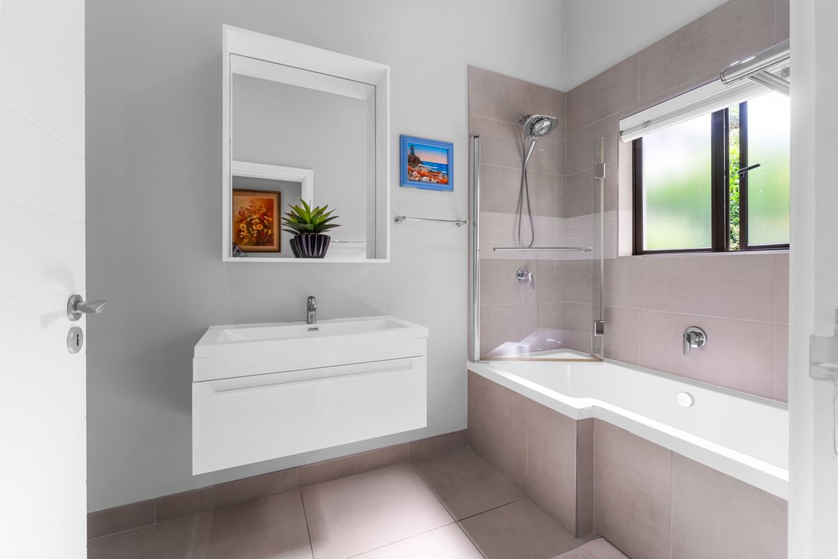 A modern bathroom featuring a wall-mounted vanity with basin, a shower-over-bath combination with glass screen, and neutral floor-to-ceiling tiling.