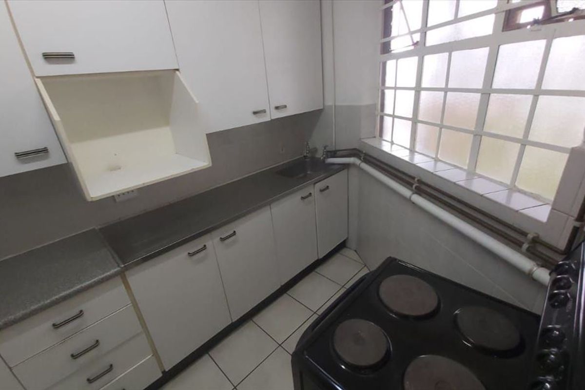 A compact kitchen featuring white cabinetry, a stainless steel sink, and a freestanding electric stove, with tiled flooring and a large window.