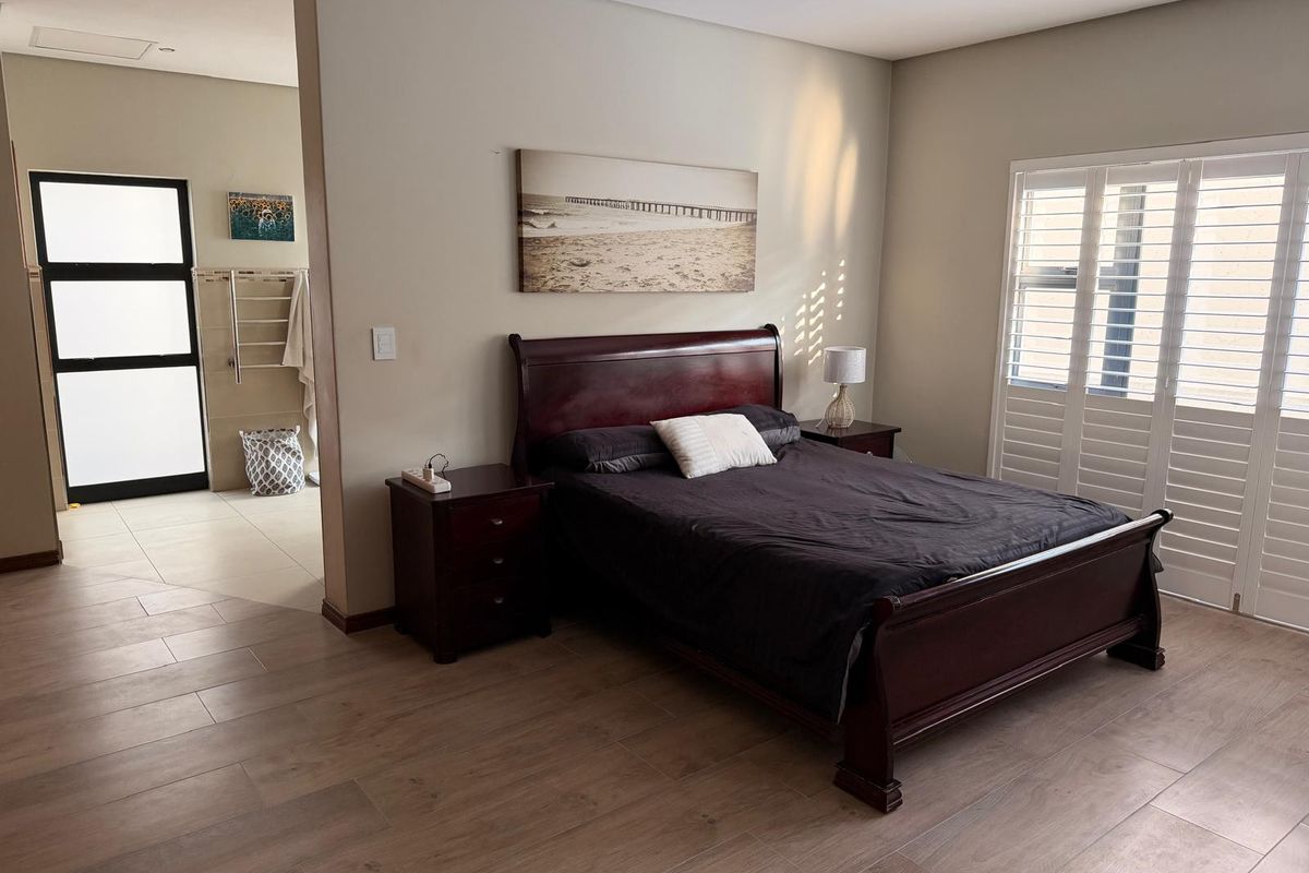 Spacious bedroom featuring wood-look tile flooring, plantation shutters, and an open-plan layout leading into an adjacent bathroom area.