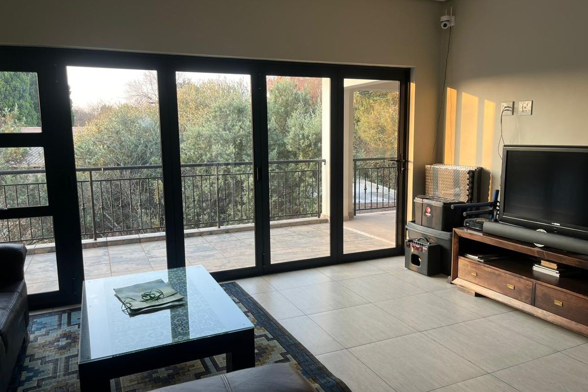 A bright living room featuring large black-framed sliding glass doors that open onto a tiled balcony with garden views.