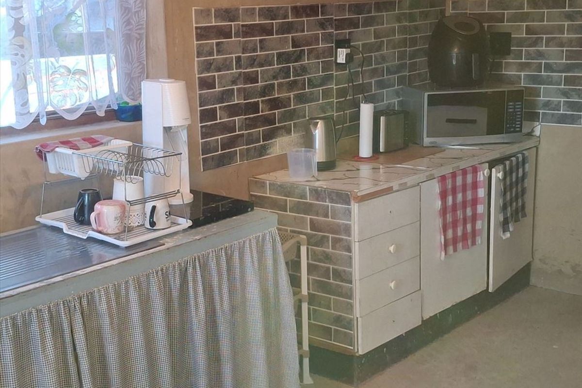 A functional kitchen area featuring tiled splashbacks, built-in cabinetry, and a stainless steel sink, offering potential for modernization and cosmetic updates.