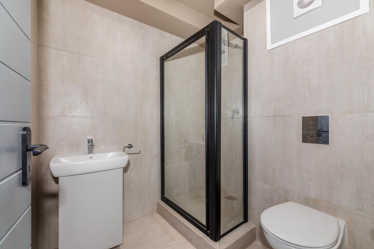 Modern bathroom featuring a glass-enclosed shower, wall-mounted toilet with concealed cistern, and a pedestal basin with neutral floor-to-ceiling tiling.
