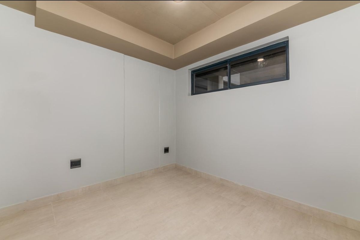 A clean, empty room featuring neutral tiled flooring, a recessed ceiling detail, and a high-set horizontal window providing natural light.