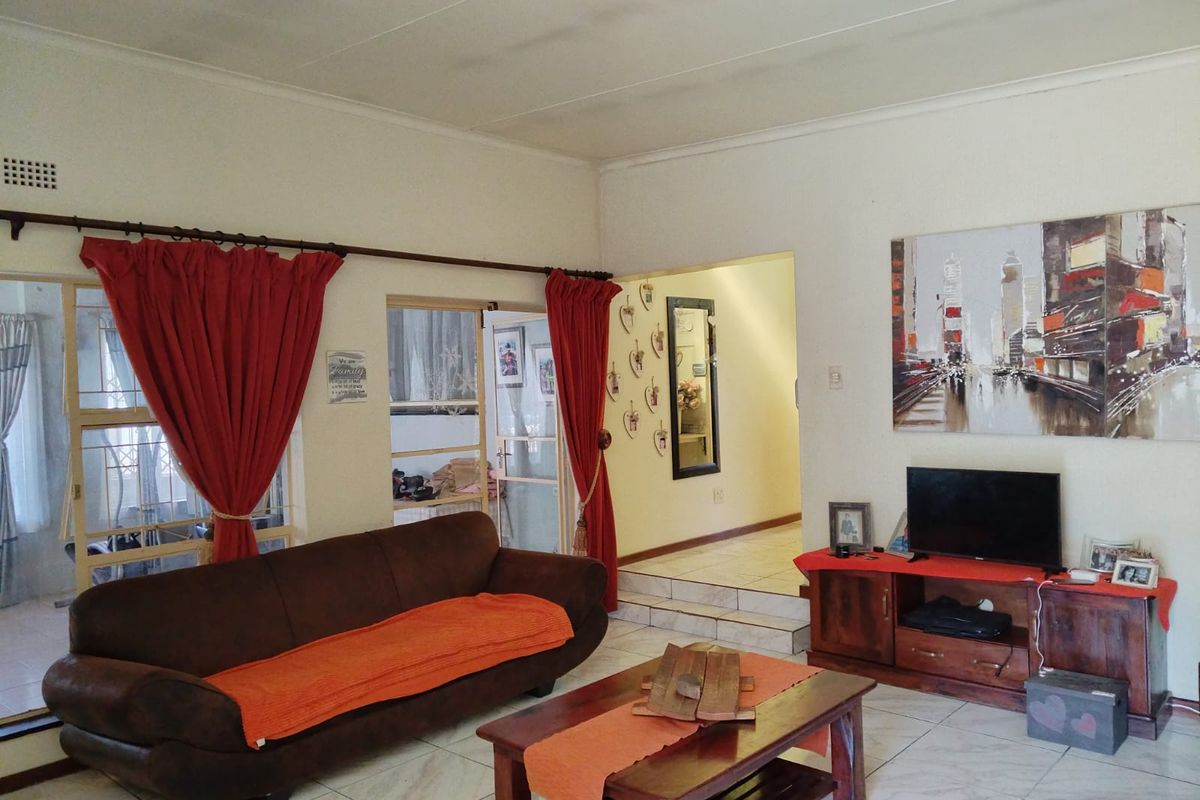 A living room featuring tiled flooring, large windows with curtain rods, and a step-up transition leading to an adjacent hallway.