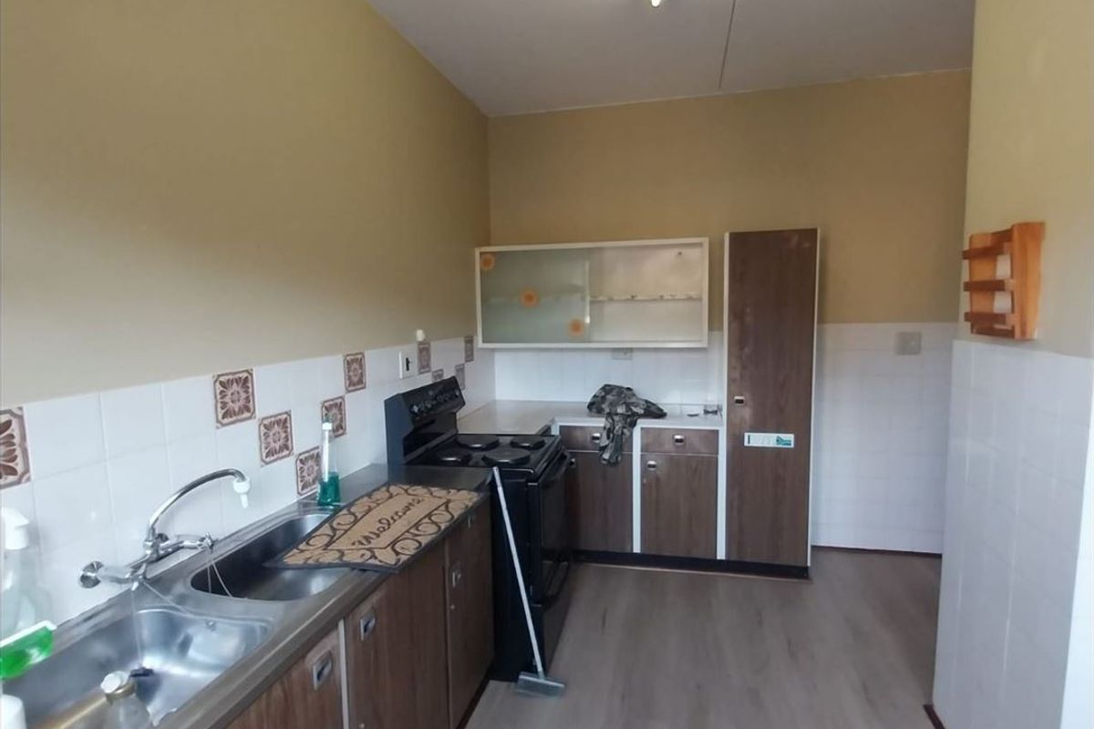 A functional kitchen featuring wood-finish cabinetry, a double stainless steel sink, tiled splashbacks, and a freestanding stove.