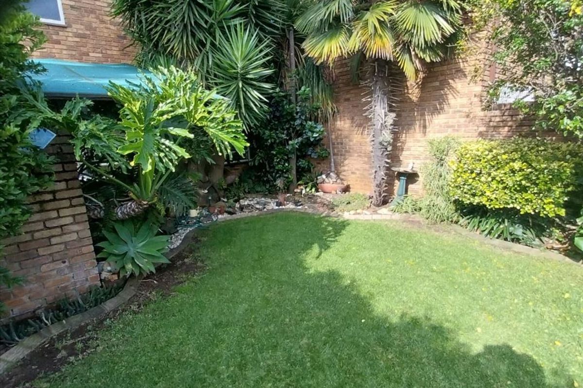 A private rear garden featuring a manicured lawn, established palm trees, and brick boundary walls, providing a secluded outdoor space.