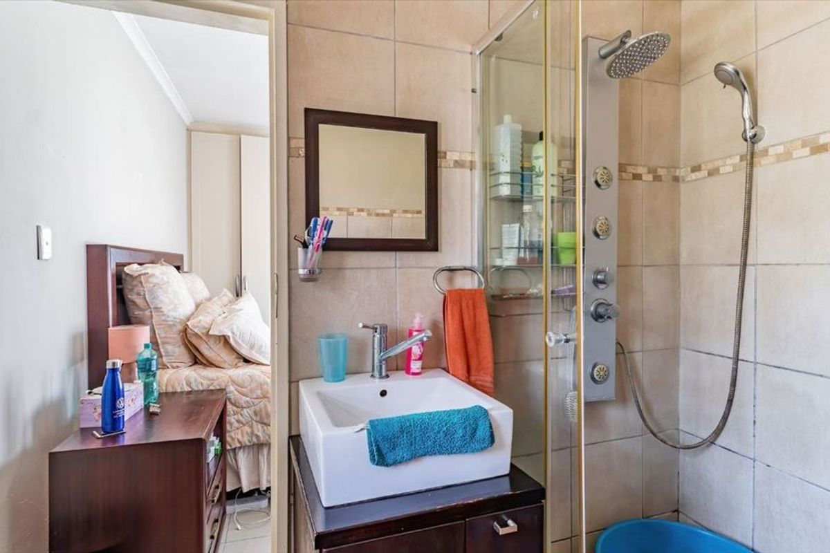 Compact en-suite bathroom featuring a modern vessel sink, vanity cabinet, and a glass-enclosed shower with a multi-jet shower panel.
