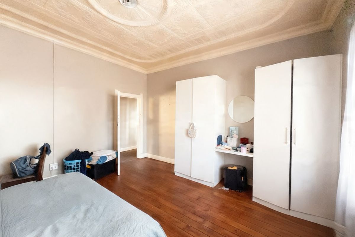 Spacious bedroom featuring original ornate pressed metal ceiling, polished timber flooring, and built-in wardrobe storage.