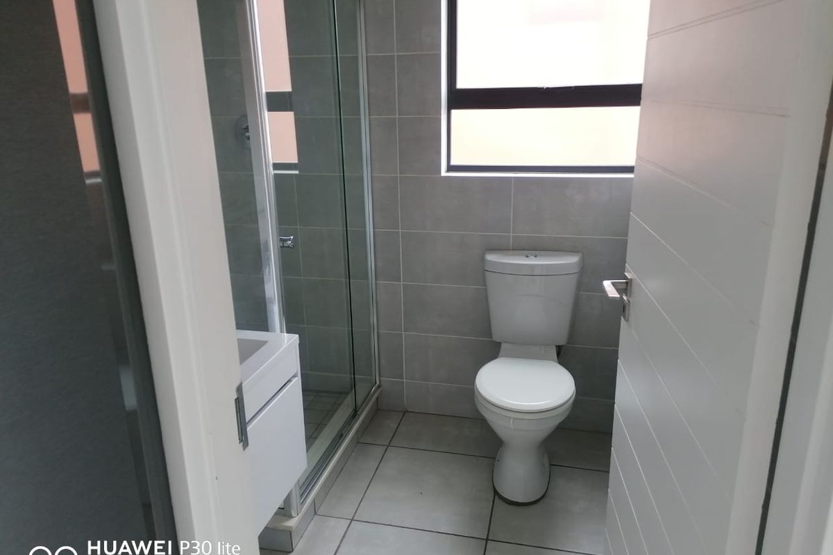 A modern bathroom featuring grey wall and floor tiles, a glass-enclosed shower, a white vanity, and a toilet.