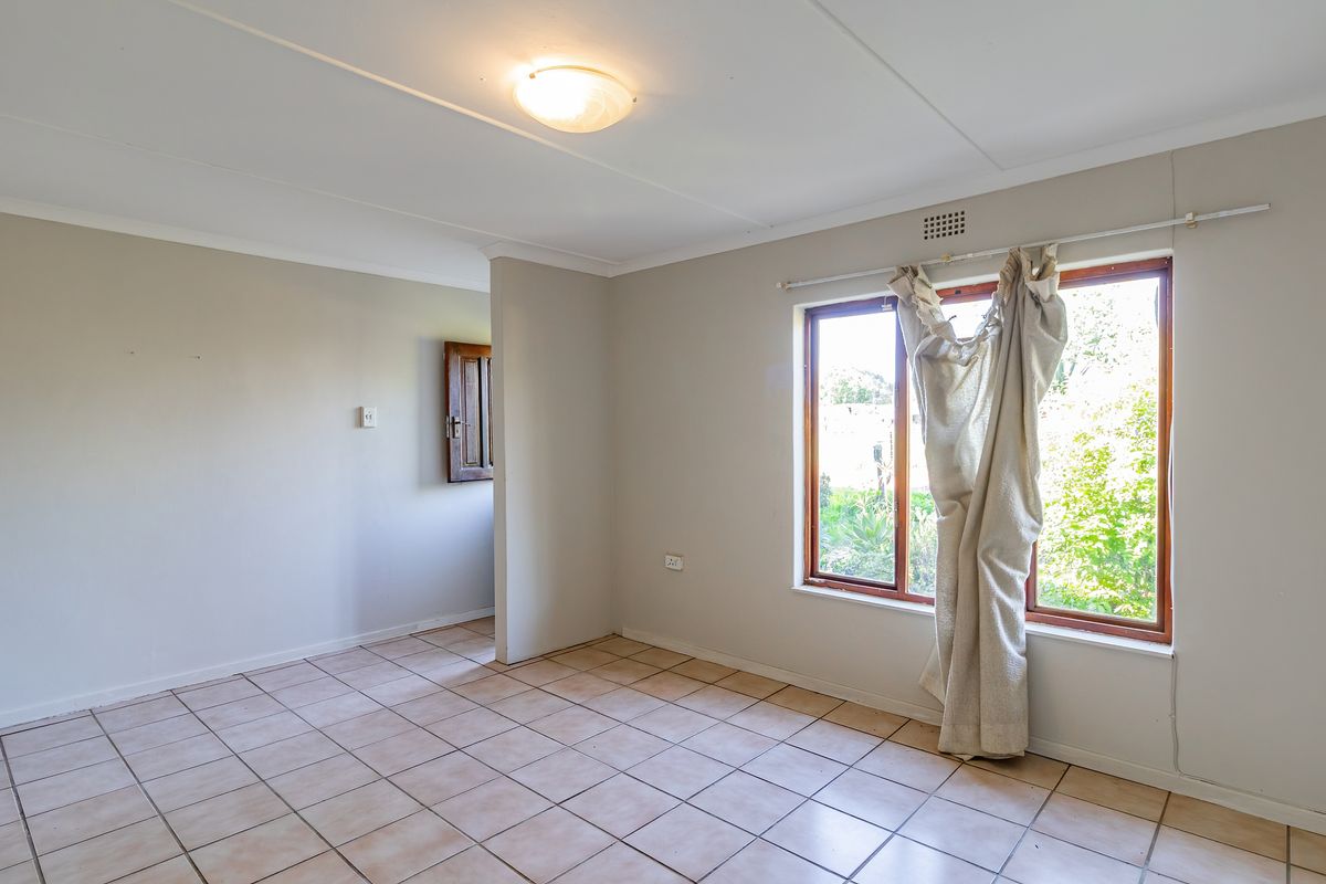 A bright, empty living room featuring neutral wall tones, tiled flooring, and a large window providing natural light and garden views.