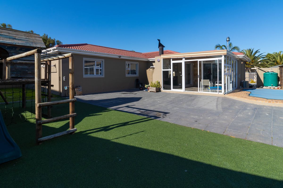 Rear exterior view featuring a paved patio area, swimming pool, and an enclosed sunroom extension attached to the main house structure.