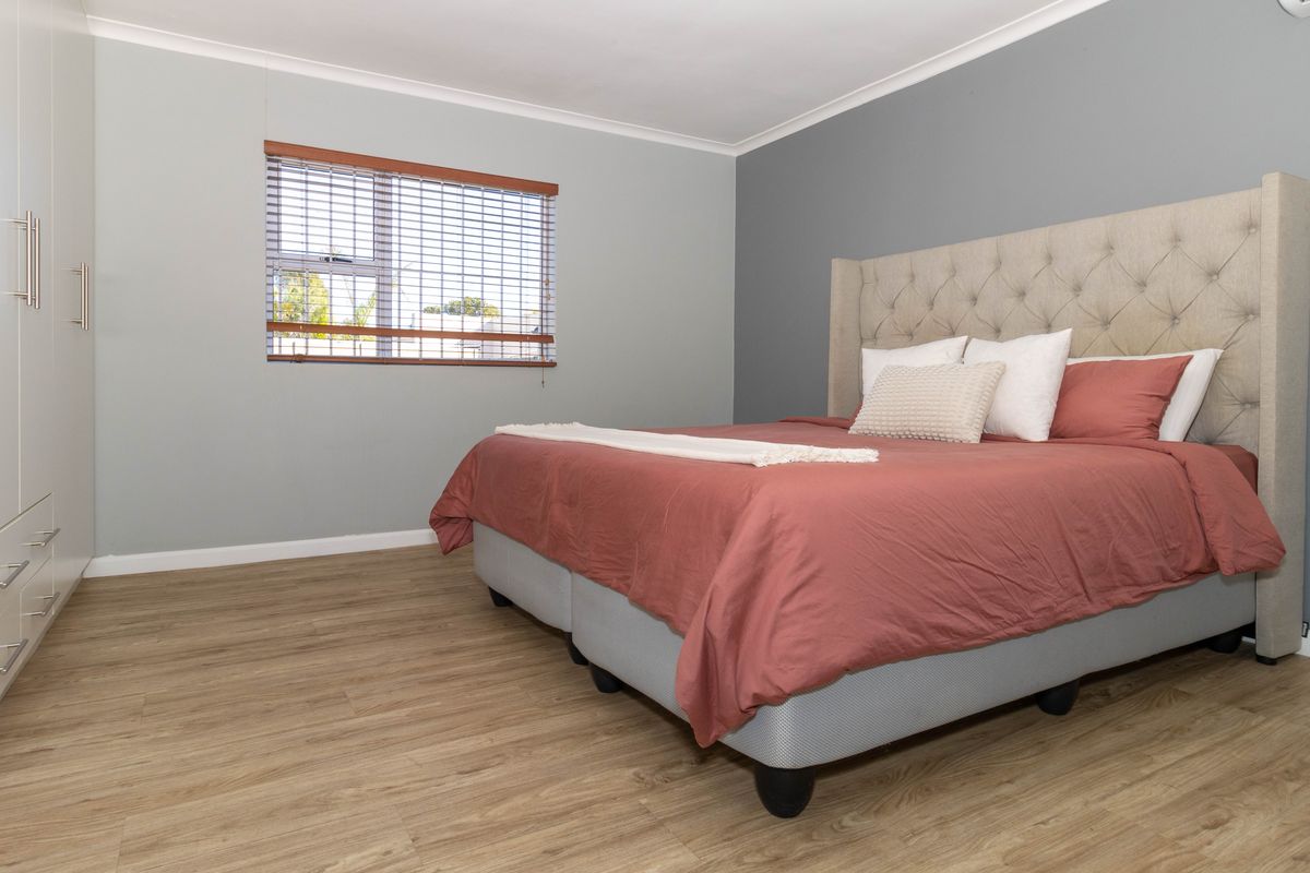 A well-maintained bedroom featuring light wood-look flooring, built-in wardrobes, and a neutral color palette with a feature wall.