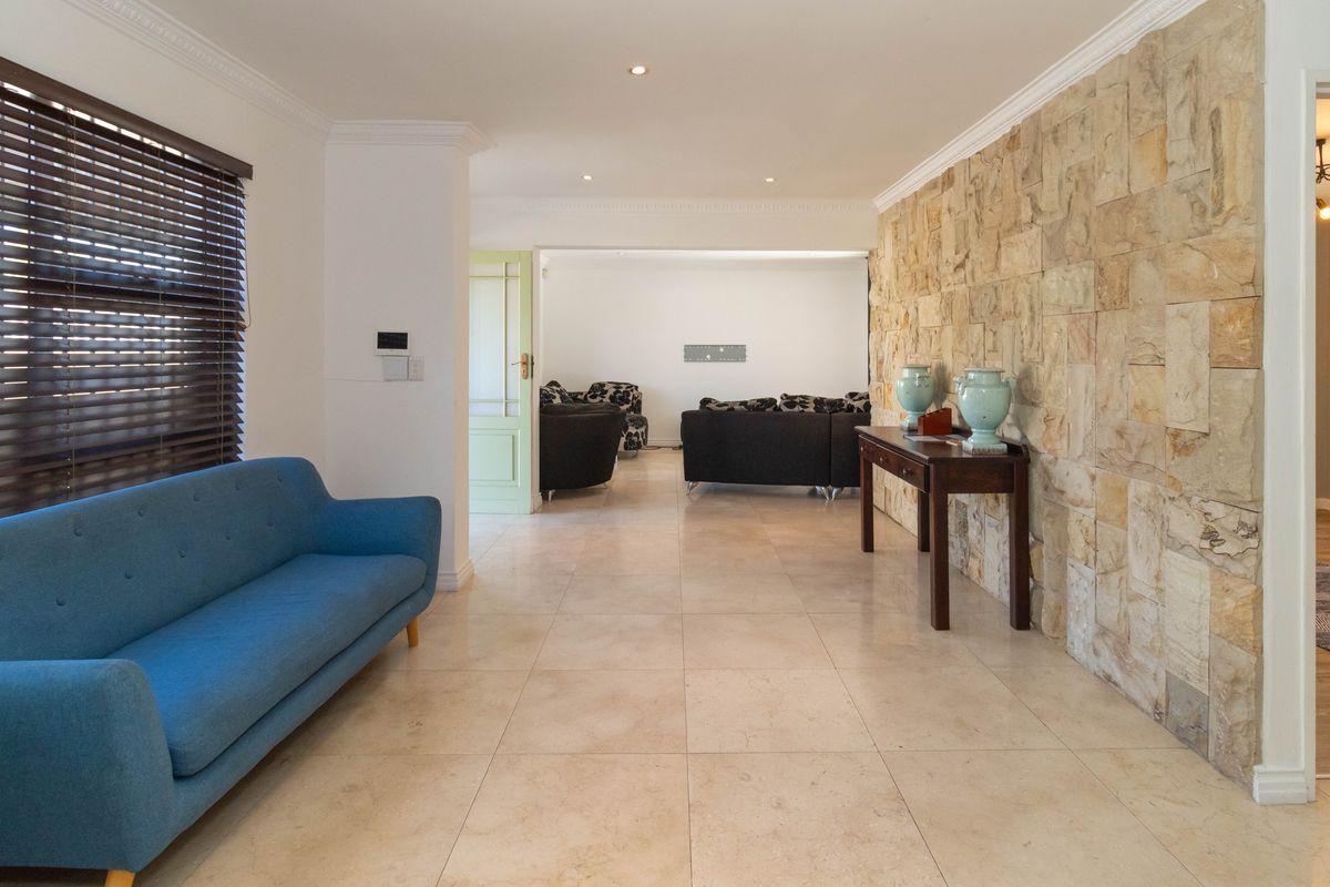 Spacious living area featuring a prominent natural stone feature wall, tiled flooring, recessed downlighting, and crown molding throughout.