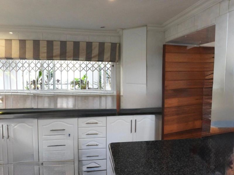A functional kitchen featuring white cabinetry, dark granite countertops, and a window with security bars, offering a clean and practical workspace.