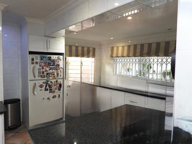 A functional kitchen featuring dark granite countertops, white cabinetry, tiled walls, and security bars on the windows.