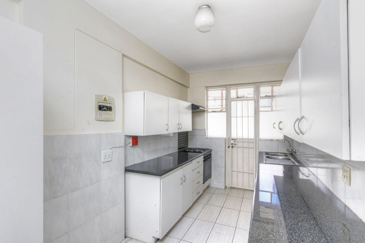 A functional galley-style kitchen featuring white cabinetry, dark granite countertops, a built-in stove, and tiled flooring with direct access to an exterior door.