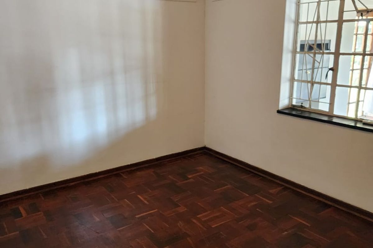 A vacant bedroom featuring traditional parquet wood flooring, a wall-mounted air conditioning unit, and a window with security bars.