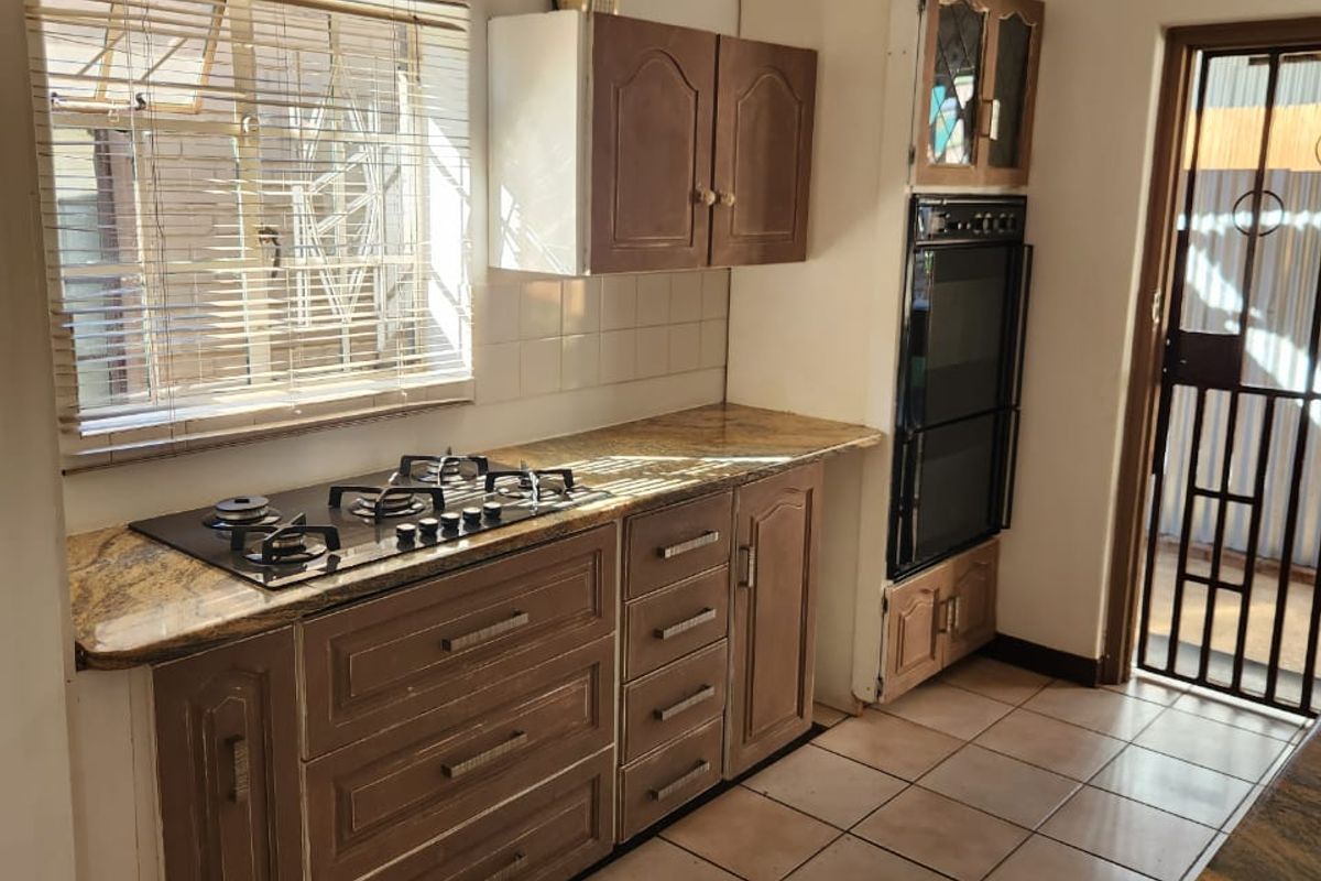A functional kitchen featuring built-in wooden cabinetry, a granite countertop, a gas hob, and a wall-mounted oven with tiled flooring.