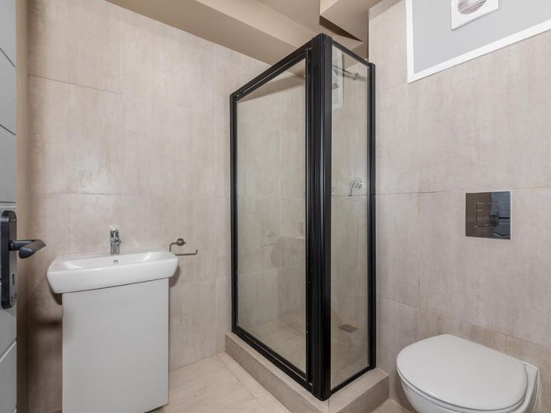 Modern bathroom featuring a glass-enclosed shower, wall-mounted toilet with concealed cistern, and a pedestal basin with neutral floor-to-ceiling tiling.